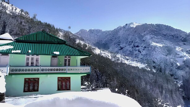 A green building with a sloped roof, surrounded by snow-covered mountains and trees.