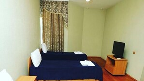 Una habitación de hotel con dos camas, un televisor sobre un soporte de madera y una cortina con estampado floral.