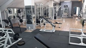 Un gimnasio con diversos equipos de ejercicio, espejos y suelo de madera.