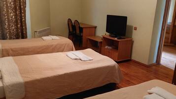 Quarto de hotel com duas camas, uma televisão sobre um suporte de madeira, uma secretária com uma cadeira e uma porta que dá para uma escadaria.