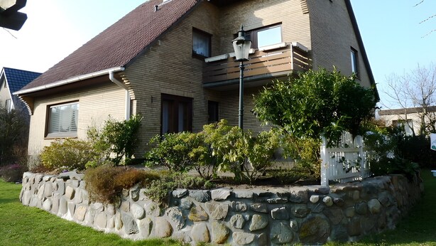 A two-story house with a stone wall and a metal fence.