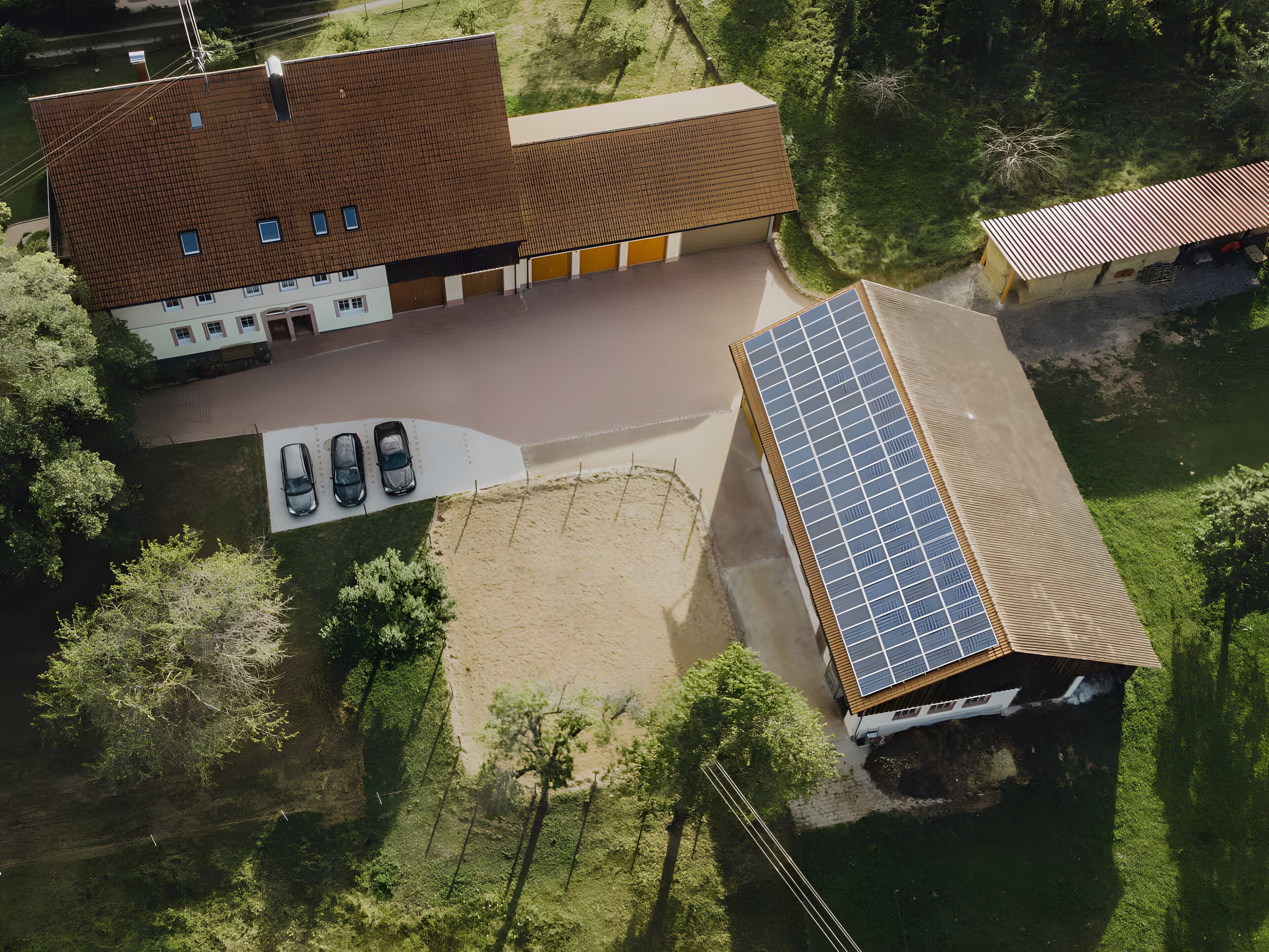 Vista aérea de um edifício com painéis solares no telhado, área de estacionamento com carros e vegetação ao redor.