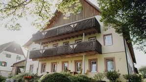 Ein mehrstöckiges Gebäude mit einem Balkon, Steinstufen und einem Garten mit einem großen Strauch.