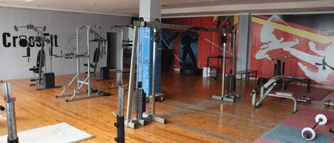 A gym with various exercise equipment, wooden flooring, and a wall with a large fitness-related mural.