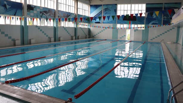 Una piscina coperta con corsie ben delimitate, ampie finestre e bandiere colorate.