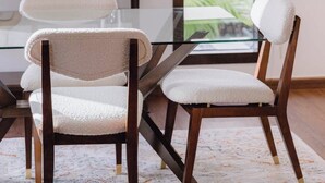 Un comedor moderno con una mesa de vidrio, dos sillas tapizadas, un jarrón con plantas y un ventanal con vistas.