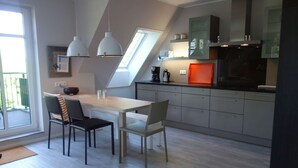 A modern kitchen with a dining area, featuring a wooden table, two chairs, pendant lights, and a built-in oven.