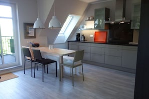 A modern kitchen with a dining area, featuring a wooden table, two chairs, pendant lights, and a built-in oven.