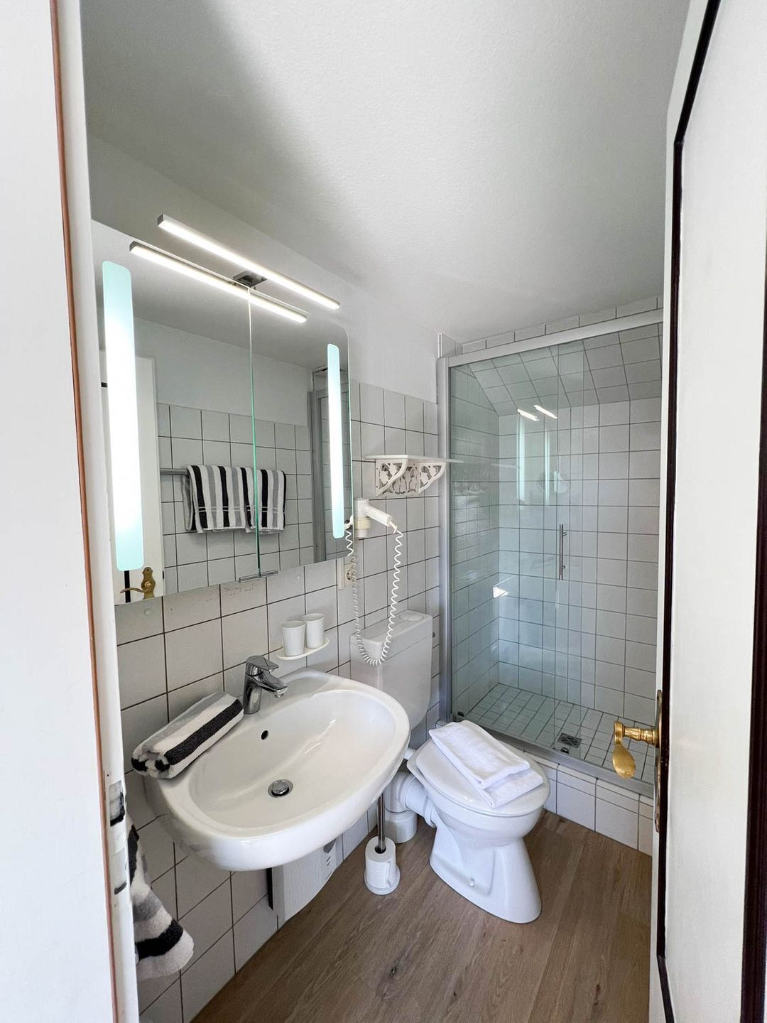A modern bathroom with a white sink, toilet, and glass shower enclosure.