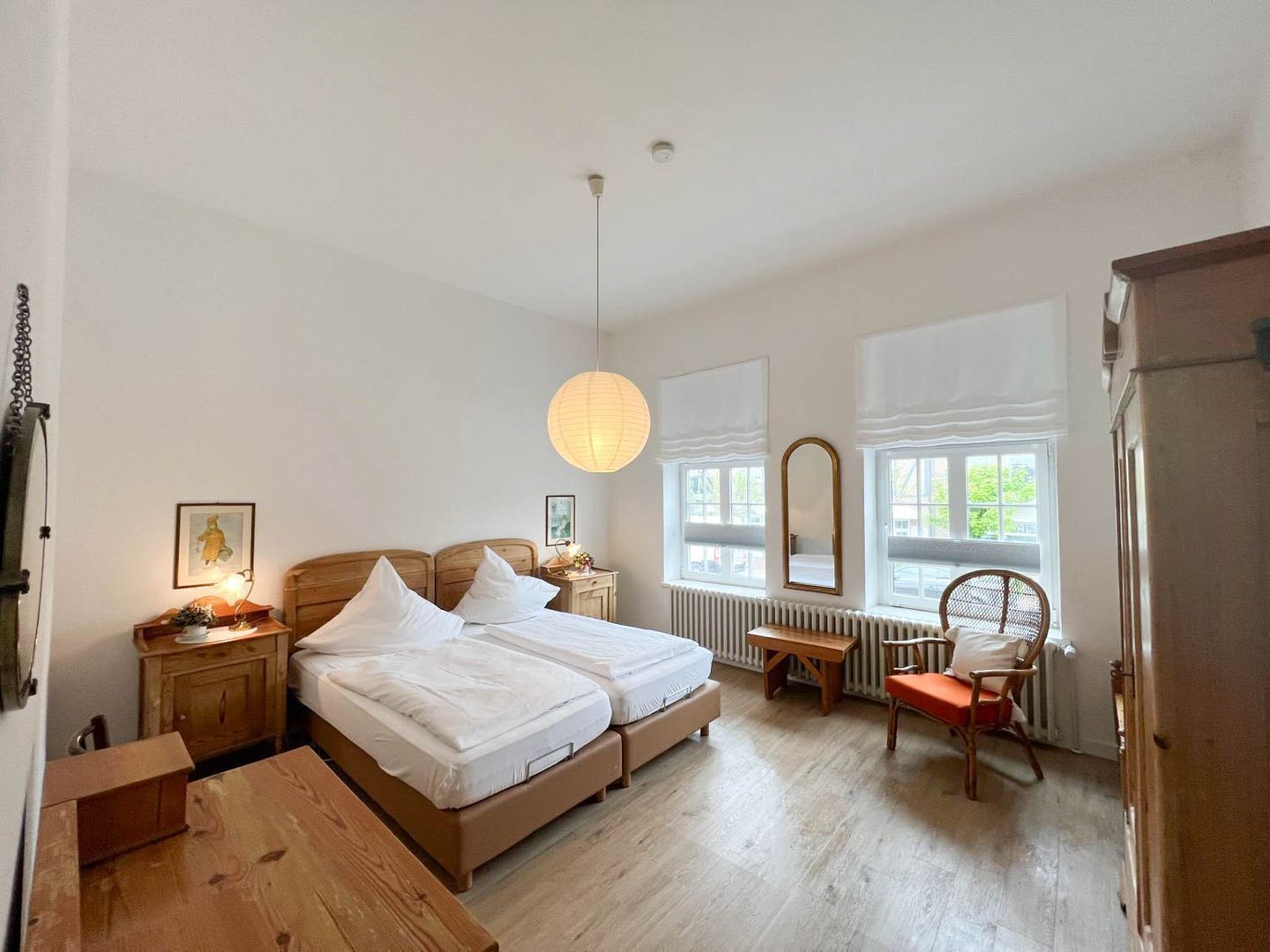 Une chambre à coucher avec un lit en bois, des tables de chevet, une chaise, un banc en bois, un luminaire suspendu et un radiateur.