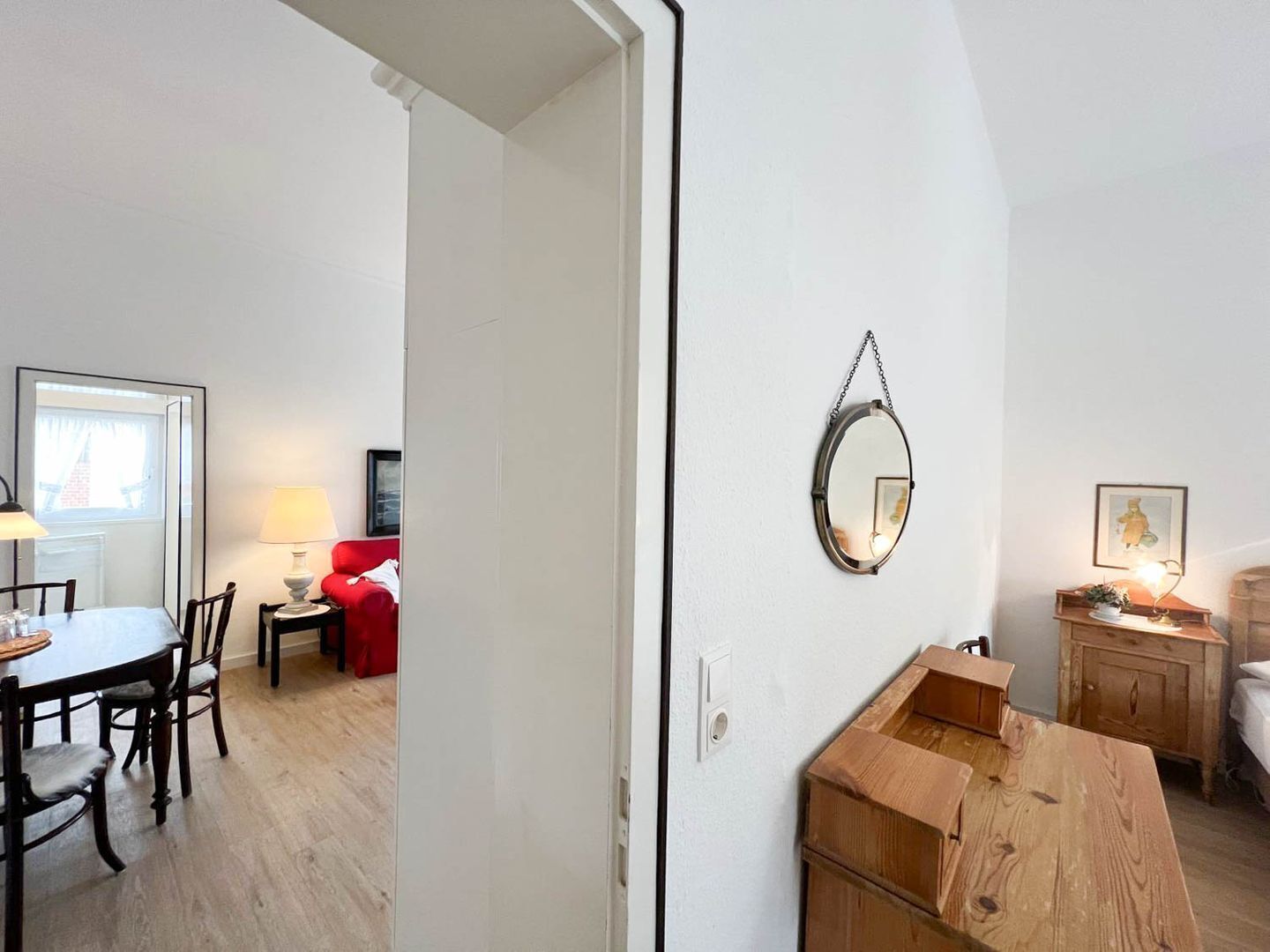 A room with a wooden dining table, chairs, a red sofa, a small table with a lamp, a wooden cabinet, and a mirror on the wall.