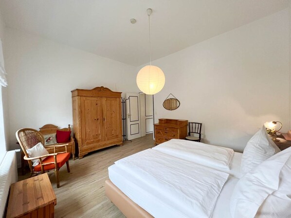 A bedroom with a large bed, wooden wardrobe, and a chair. - Haus Friesland - Apartment 2 - Spacious and elegant urban villa (Sylt)