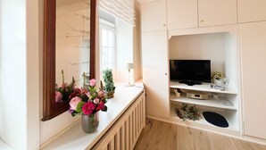 A room with a large mirror, a radiator, a TV on a shelf, and a vase of flowers. - House Friesland - Apartment 3 - An urban villa with spacious and tasteful (Sylt)