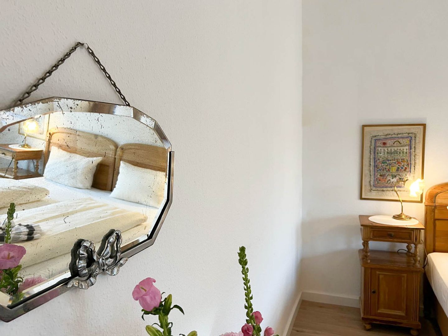A bedroom with a bed, a wooden nightstand, a bedside table, a mirror, and a framed picture on the wall.