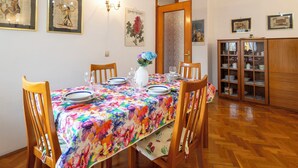 A dining room with a floral tablecloth, wooden chairs, a cabinet with glass doors, and wall-mounted artwork. - Monte Livrio by Interhome (Bormio)