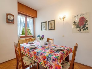 A dining area with a floral tablecloth, wooden chairs, a clock, and artwork on the walls.