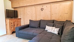 Una sala de estar acogedora con un sofá seccional gris, un mueble de madera con un televisor y una decoración con forma de corazón en la pared.