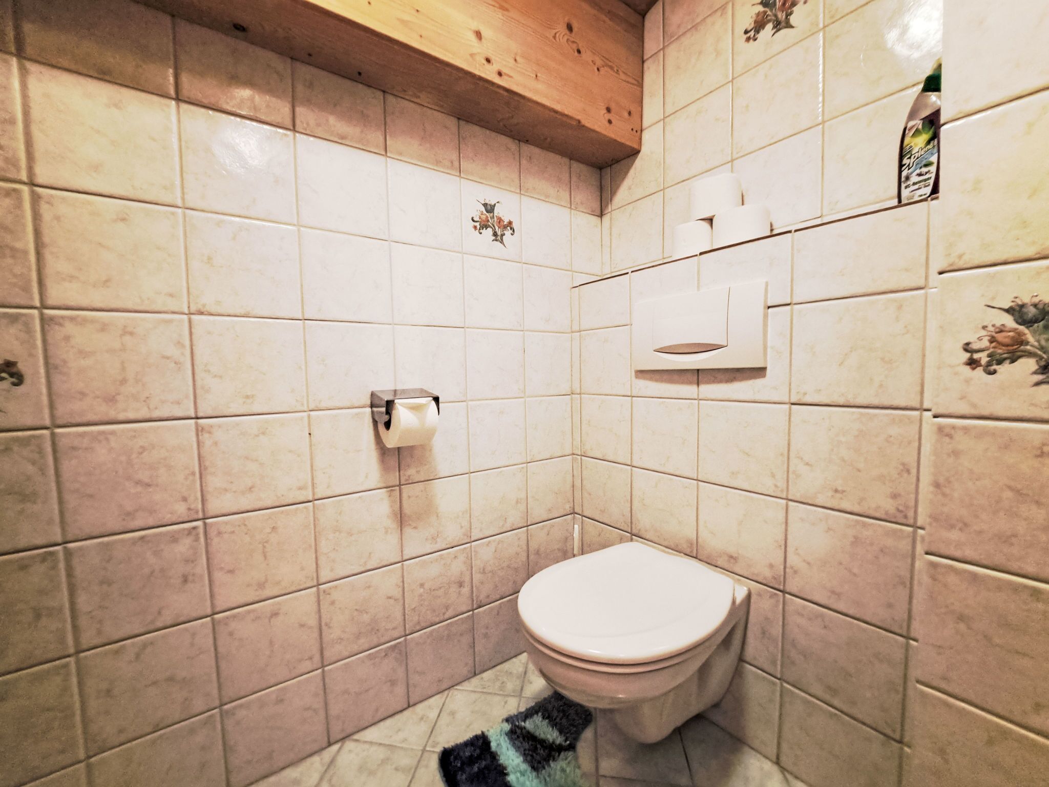 Une petite salle de bain avec des toilettes, un rouleau de papier toilette et un sèche-mains fixé au mur.