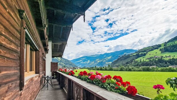 Un balcon en bois offrant une vue sur un champ verdoyant et des montagnes.