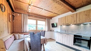 L’intérieur chaleureux d’un chalet avec un plafond en bois, un coin repas comprenant une table et des chaises, une cuisine dotée de meubles en bois et d’un four encastré, et une fenêtre agrémentée de rideaux.
