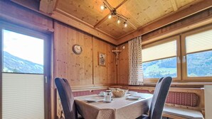 Une salle à manger en bois, avec une table dressée pour deux personnes, un banc et une vue sur les montagnes grâce à de grandes fenêtres.