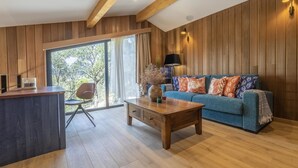 Un salon moderne avec un plafond en bois, un canapé bleu agrémenté de coussins à motifs, une table basse en bois et une grande fenêtre avec des rideaux.