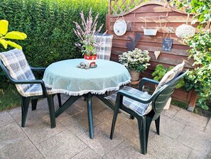 Une terrasse extérieure avec une table ronde, deux chaises et un pot de fleurs.