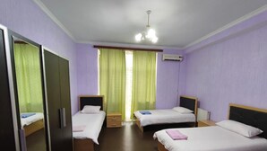 A hotel room with four single beds, a wardrobe, a mirror, and a ceiling fan.