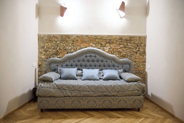 Quarto com parede de pedra, cabeceira estofada e sofá estampado.