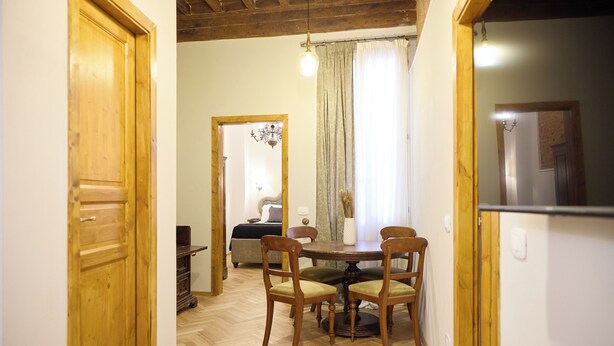 Un coin repas avec une table et des chaises en bois, un lustre et une vue sur une chambre à coucher avec un lit et des rideaux.