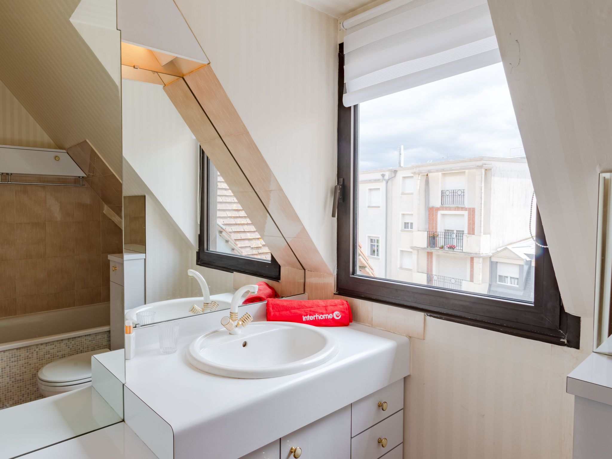 Een moderne badkamer met dakraam, witte sanitair en uitzicht op gebouwen door een raam.