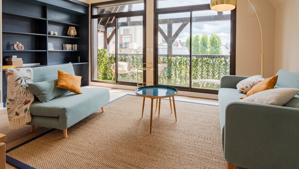 Un soggiorno moderno con soffitto alto, ampie finestre e vista su un balcone.