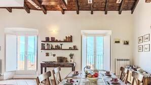 A dining area with a wooden table, chairs, and a view through large windows. - Laghina by Interhome (Musso)