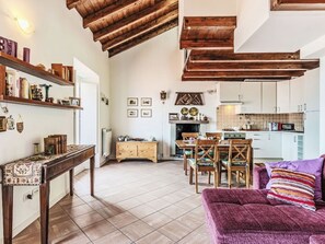 Un vaste espace de vie doté d’un plafond haut, de poutres en bois, d’une table à manger avec des chaises, d’un canapé et d’une cuisine à l’arrière-plan.