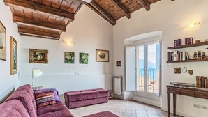 A living room with a large sofa, a smaller sofa, a table with books, and a view of the sea through a balcony door. - Laghina by Interhome (Musso)