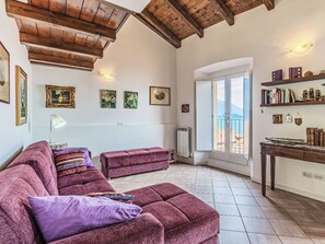 Un salon comprenant un grand canapé, un canapé plus petit, une table avec des livres et une vue sur la mer, visible à travers une porte-fenêtre donnant sur un balcon.
