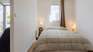 A small, well-lit bedroom with a bed, two bedside tables with lamps, a window with curtains, and a view of the outdoors. - Cabourg Plage by Interhome (Cabourg)