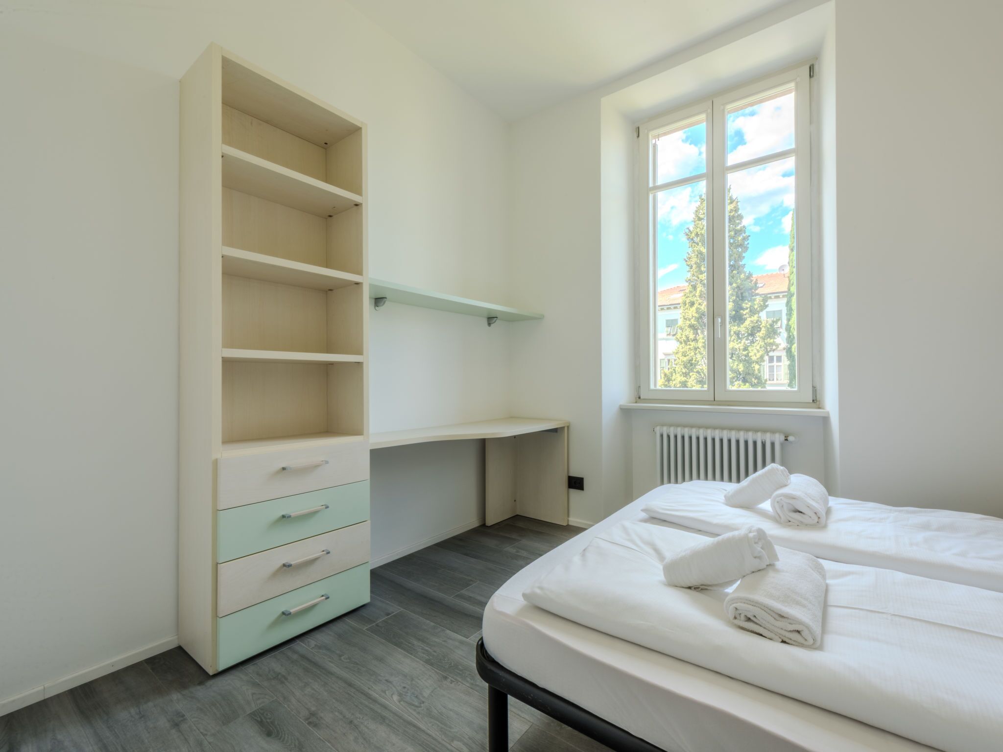Une chambre à coucher comprenant un lit, une armoire intégrée, une fenêtre et un radiateur.