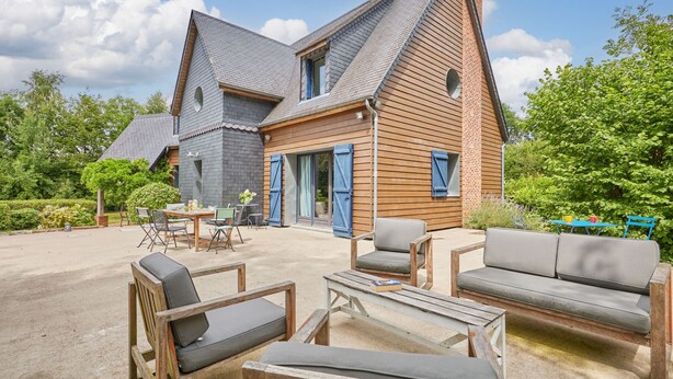 A two-story house with a sloped roof, a wooden exterior, and a patio area with outdoor furniture.