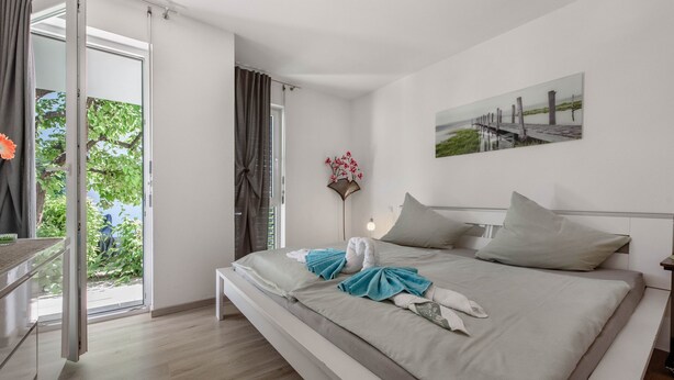 Un dormitorio moderno con una cama, un cuadro y vistas a la vegetación por una puerta abierta.