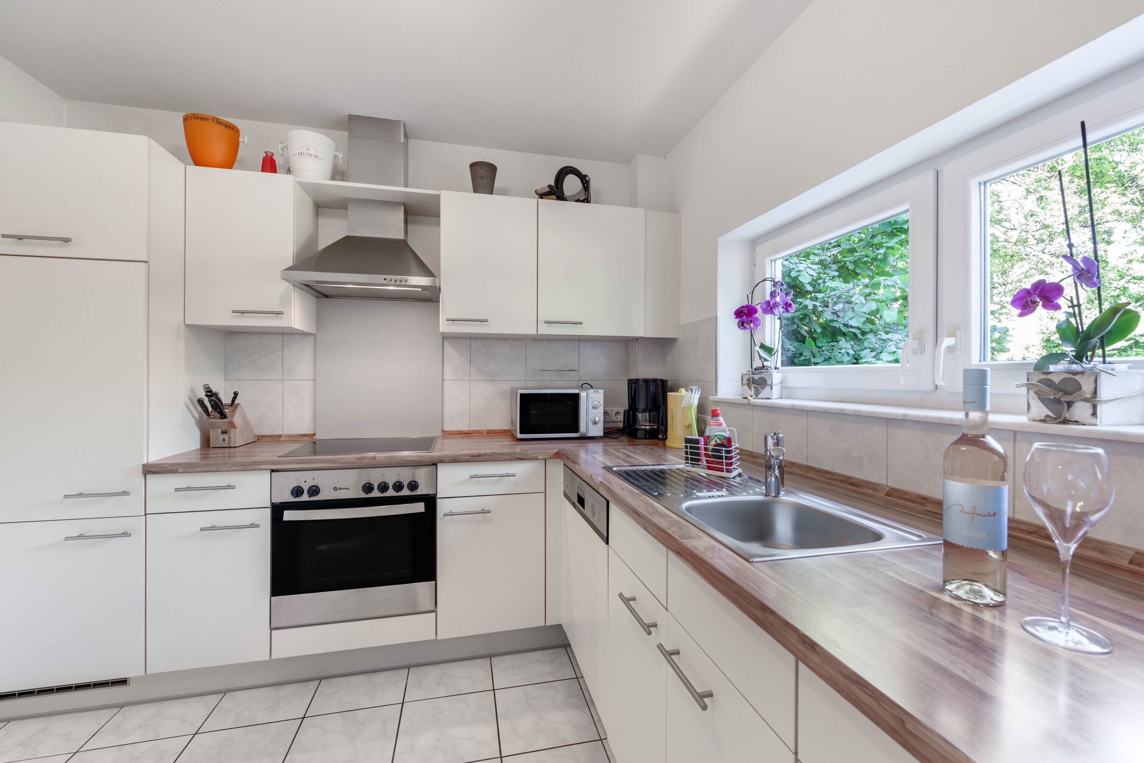 A modern kitchen with white cabinets, a stainless steel range, a microwave, and a window with a view of greenery.