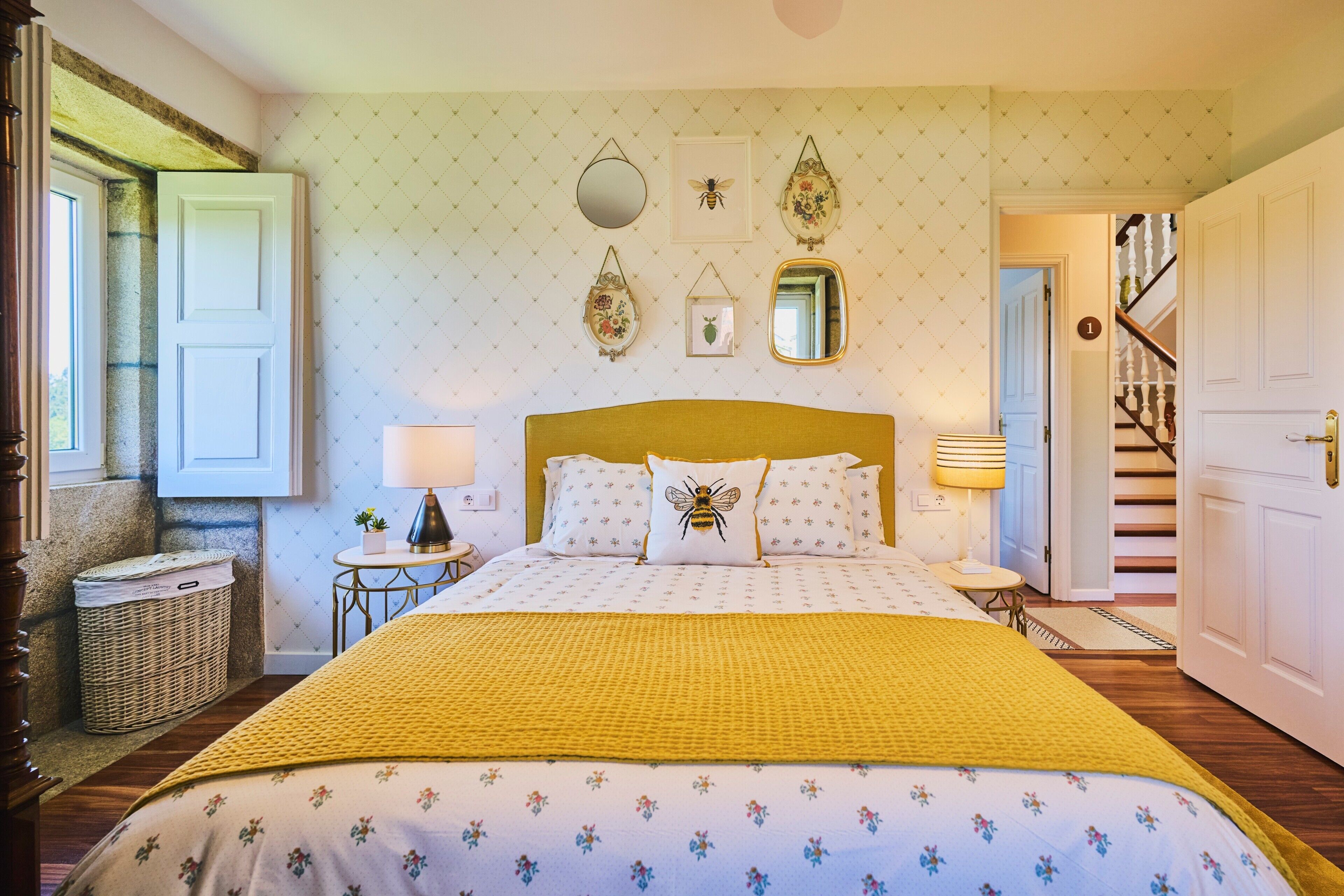A bedroom with a bed, a bedside table, a lamp, a mirror, and a door leading to a staircase.