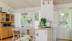 A bright kitchen with white cabinets, a dining table with chairs, and a wicker chair with a green cushion.
