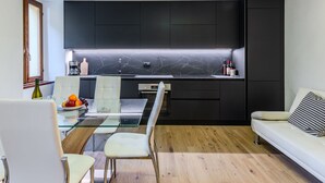 A modern kitchen with dark cabinets, a marble backsplash, and a glass dining table with chairs. - La Scaletta by Interhome (Dongo)