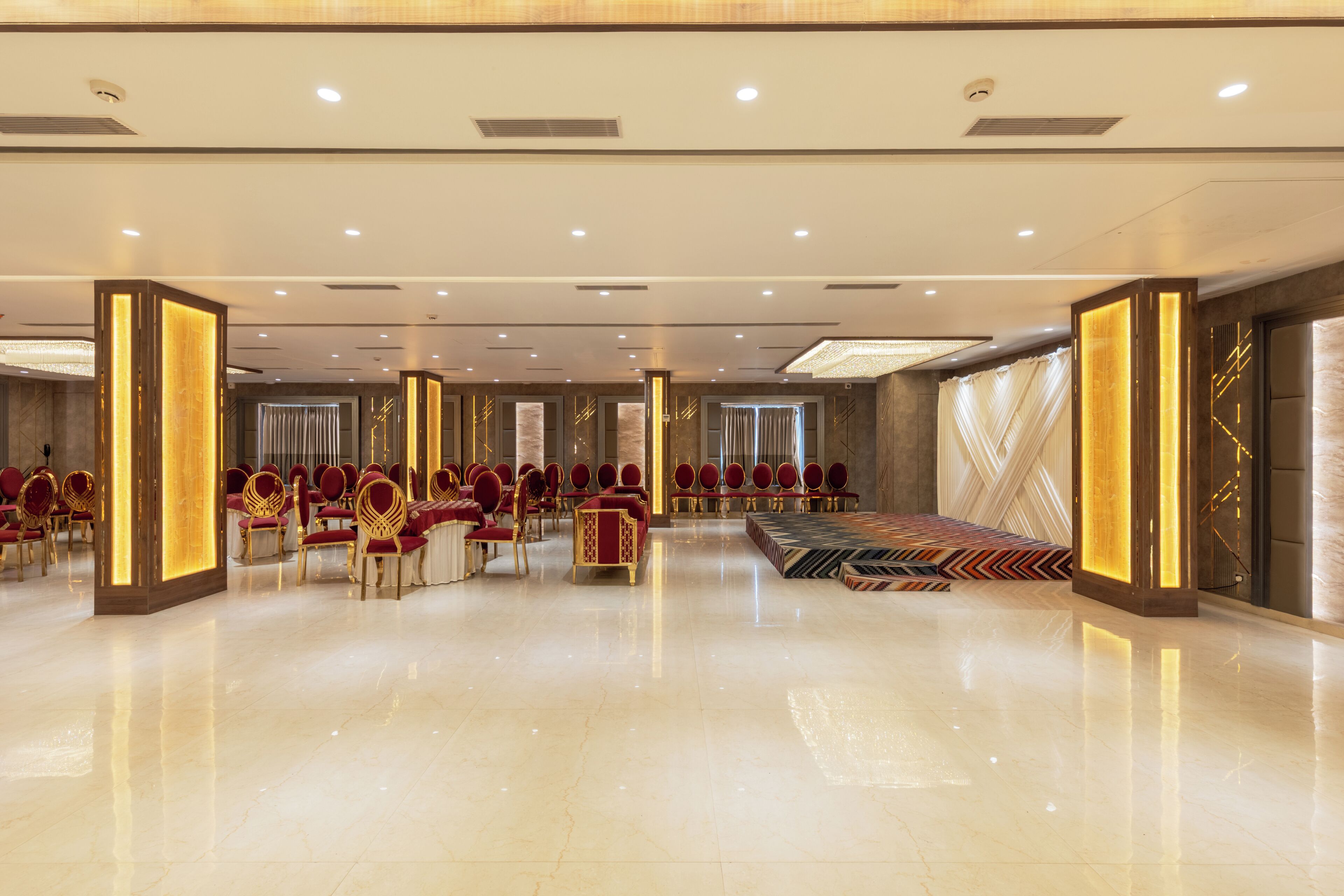 Un hall d’hôtel spacieux, avec des rangées de fauteuils rouges et dorés, un espace salon central et une moquette à motifs.
