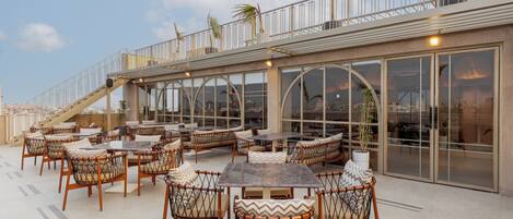 An outdoor seating area with tables and chairs, a staircase, and large windows.