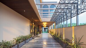 A modern hotel corridor with a checkered floor, potted plants, and a decorative metal railing. - Hotel Royal Bagh - Opposite City Park (Jaipur)