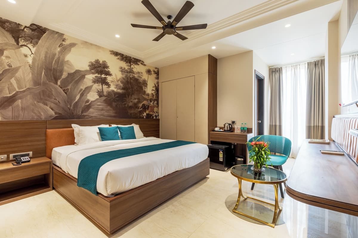 Ein modernes Hotelzimmer mit einem großen Bett, einem Schreibtisch, einem Stuhl, einem kleinen Tisch mit einer Vase und einem Deckenventilator.