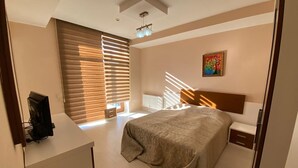 A bedroom with a bed, bedside tables, a desk, and a window with blinds.