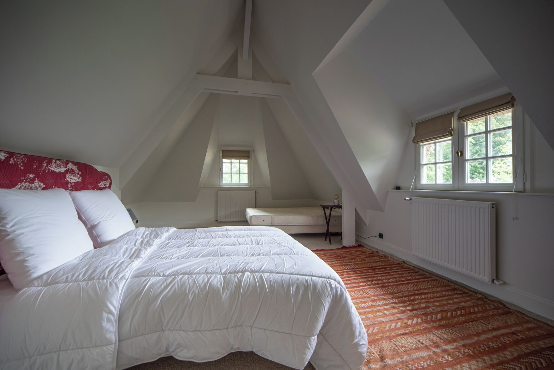 A bedroom with a large bed, a small table, a window, and a radiator.